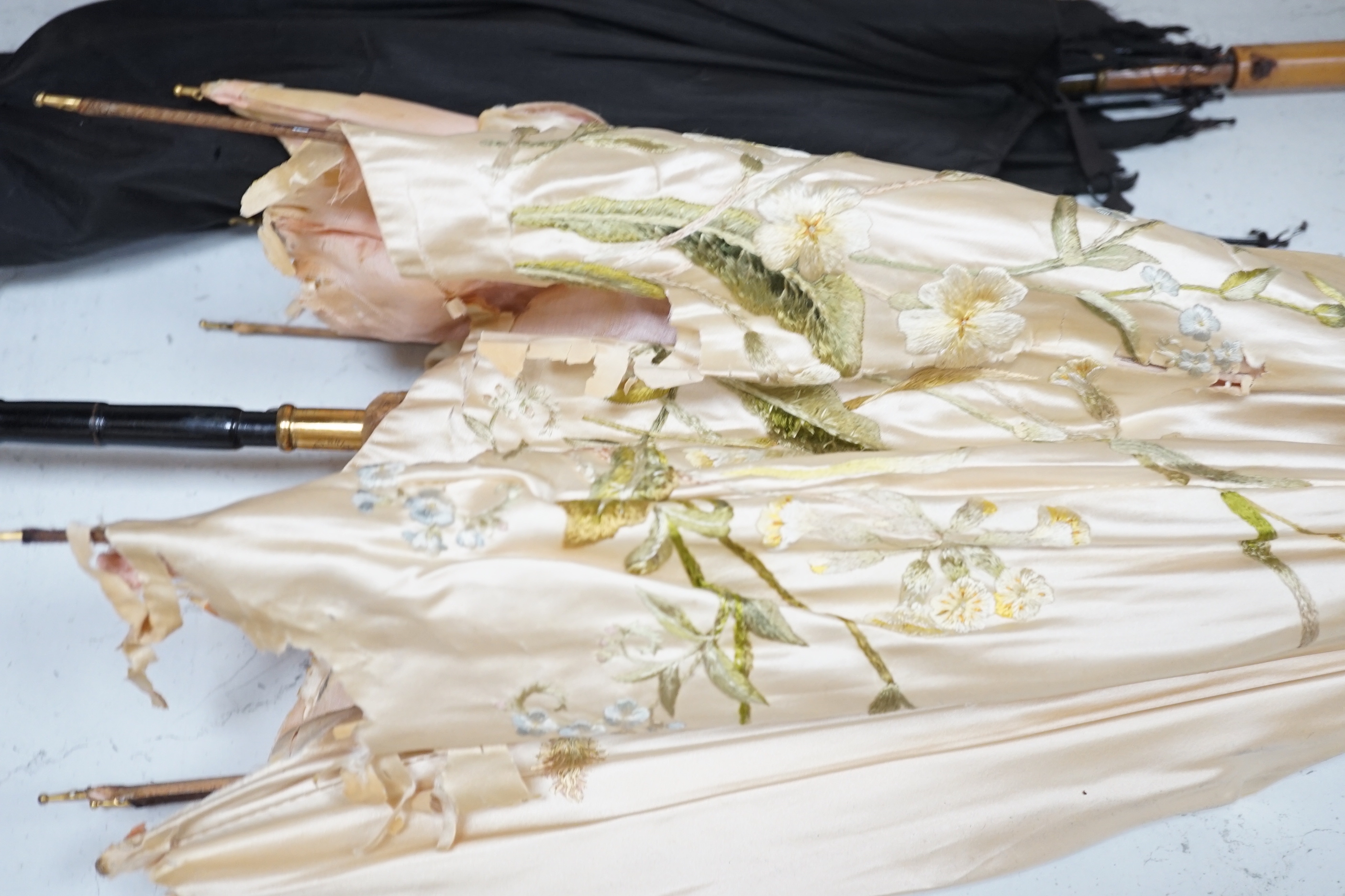 A cream silk embroidered ladies parasol with porcelain handle and a black silk umbrella with silver top (both badly torn)